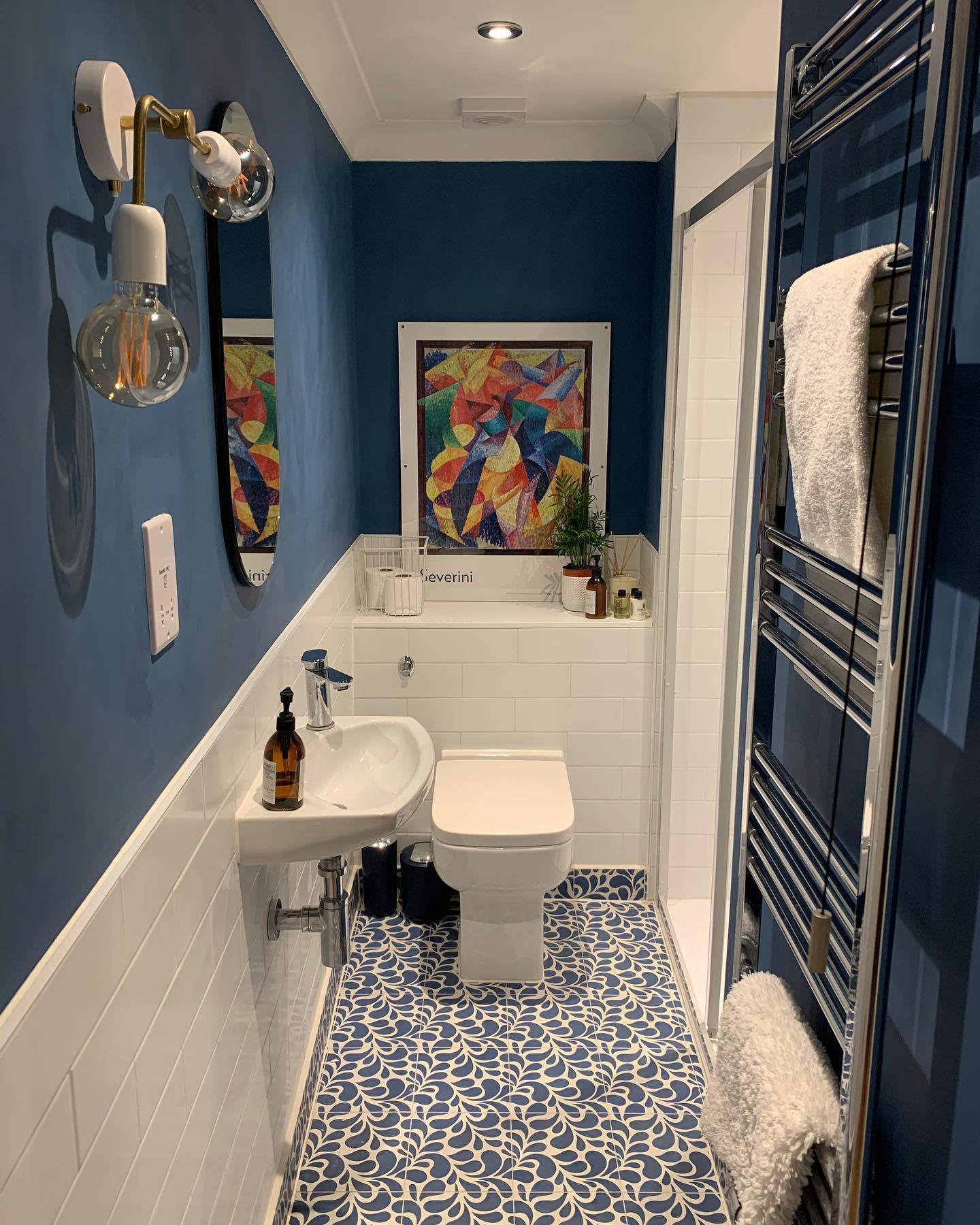 Modern blue bathroom with abstract art, patterned floor tiles, and wall-mounted towel rail.